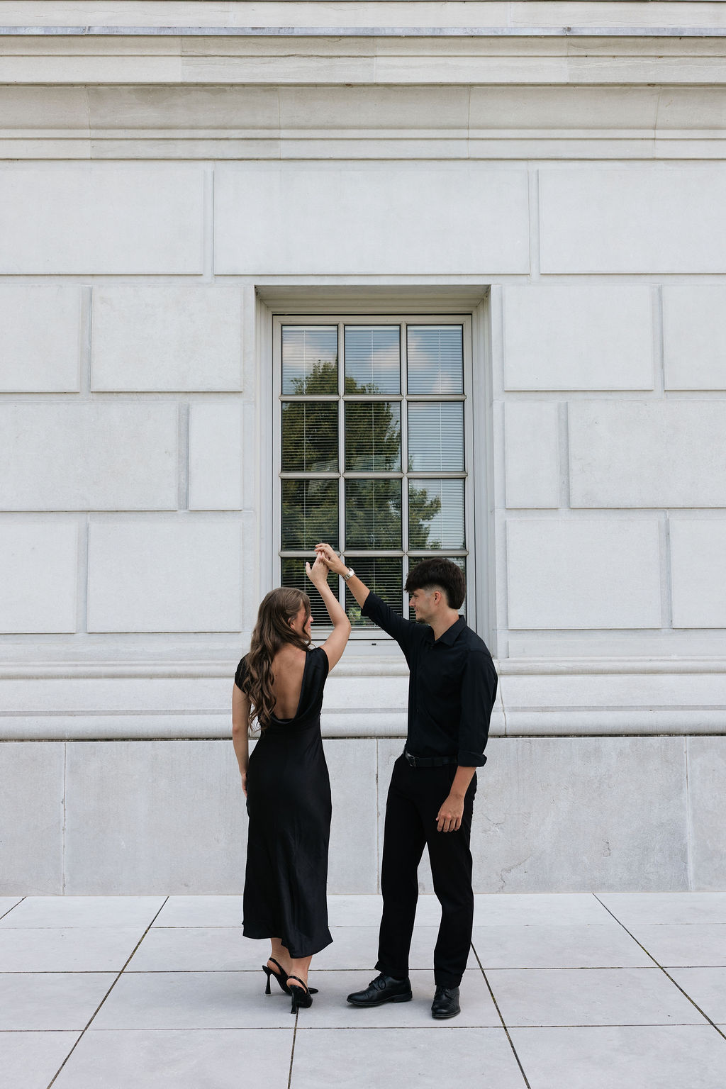 Max turning Angela under his arm outside a limestone building