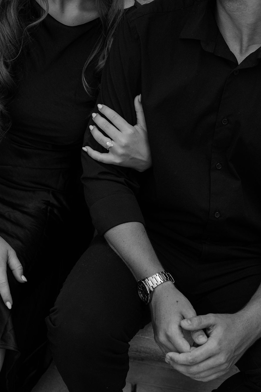 Angela's hand, wearing her engagement ring, resting on Max's arm